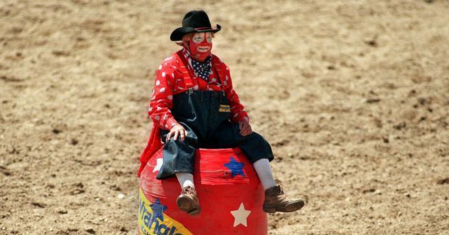 Caption: Rodeo Clown Quail Dobbs jokes with the announcer while he waits  atop his Wrangler barrel for the next bull and cowboy duo to come out of  the chutes. Photographer: Eric Lutzens